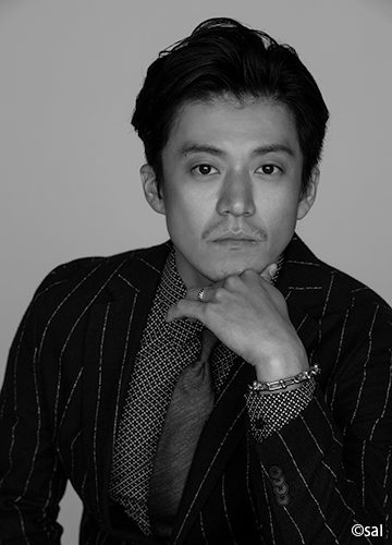 회색 배경 앞에서 손을 턱에 괴고 카메라를 바라보는 오구리 슌의 트라이스톤 엔터테인먼트 공식 프로필 사진